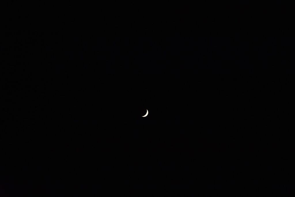 A serene crescent moon floating in a vast and dark night sky, creating a peaceful celestial scene.