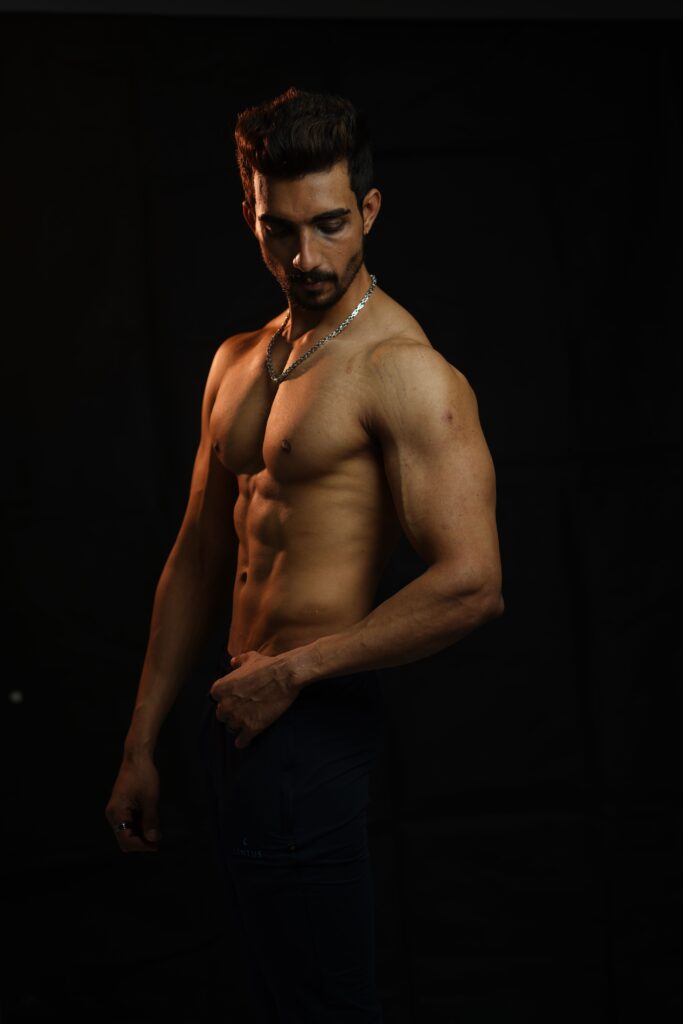 Shirtless muscular man posing in a dark studio with dramatic lighting.