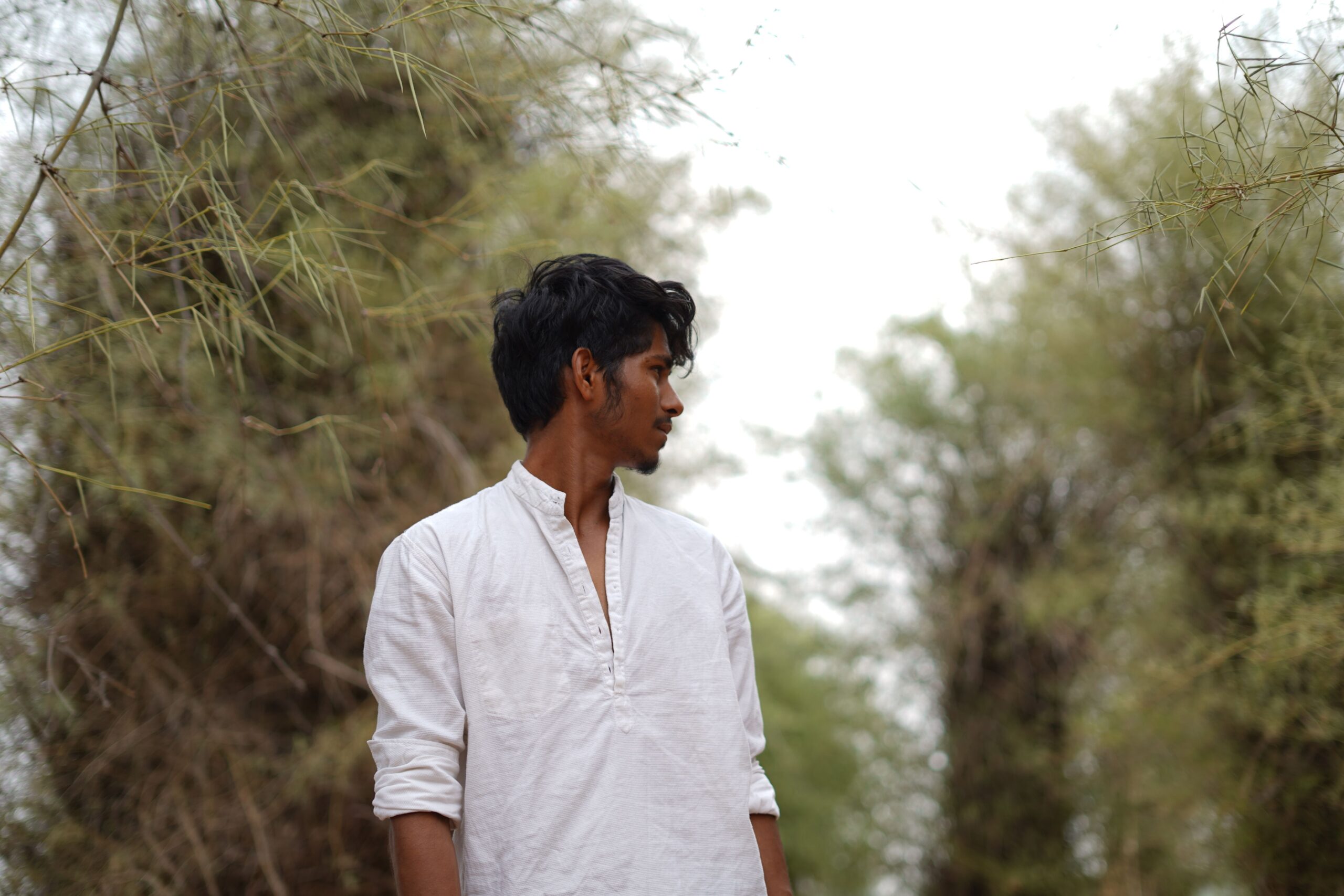 A young man in a white shirt gazes into the distance, surrounded by lush greenery.